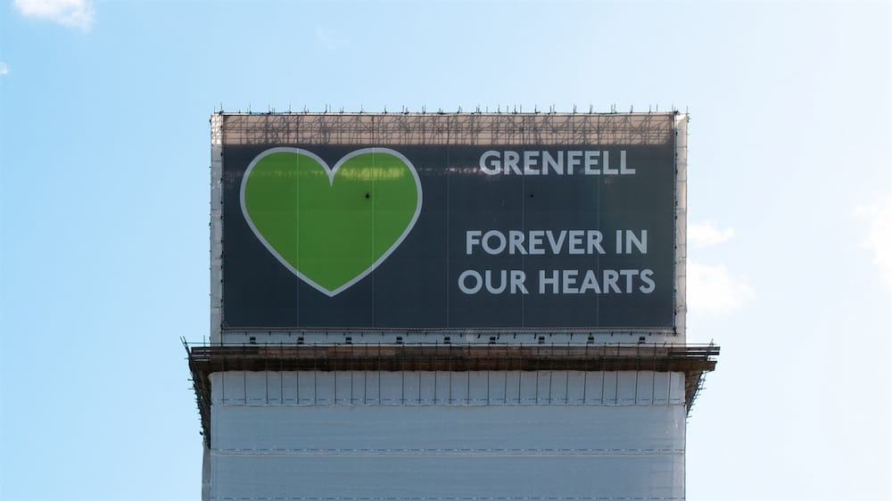 An image of Grenfell Tower, showing a banner with a green heart and text that reads 'Grenfell Forever in our hearts'