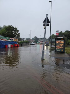 A road with flood water affects a shop and a bus stop