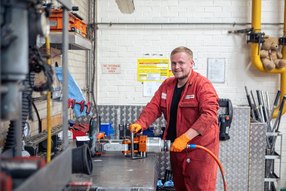 A member of Transport, engineering and workshops in red overalls using a tool at a work bench