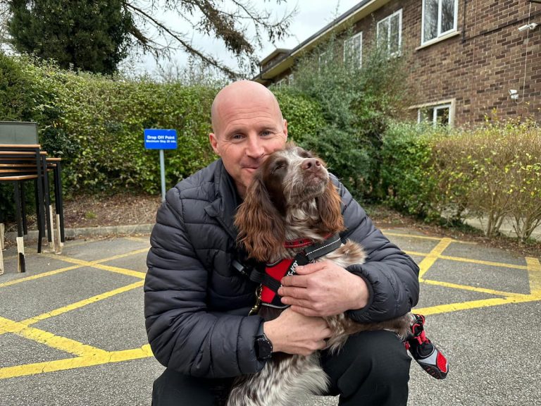 Fire Investigator Alex Daw, crouching down hugging Giddy, the fire investigation dog.