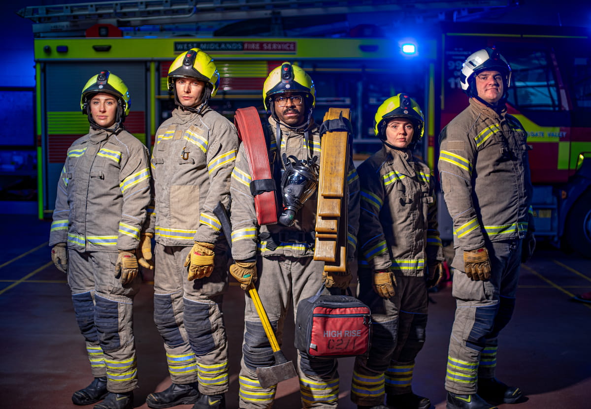 A shot of of five firefighters stood in a line in PPE, with the firefighter in the centre carrying lots of equipment