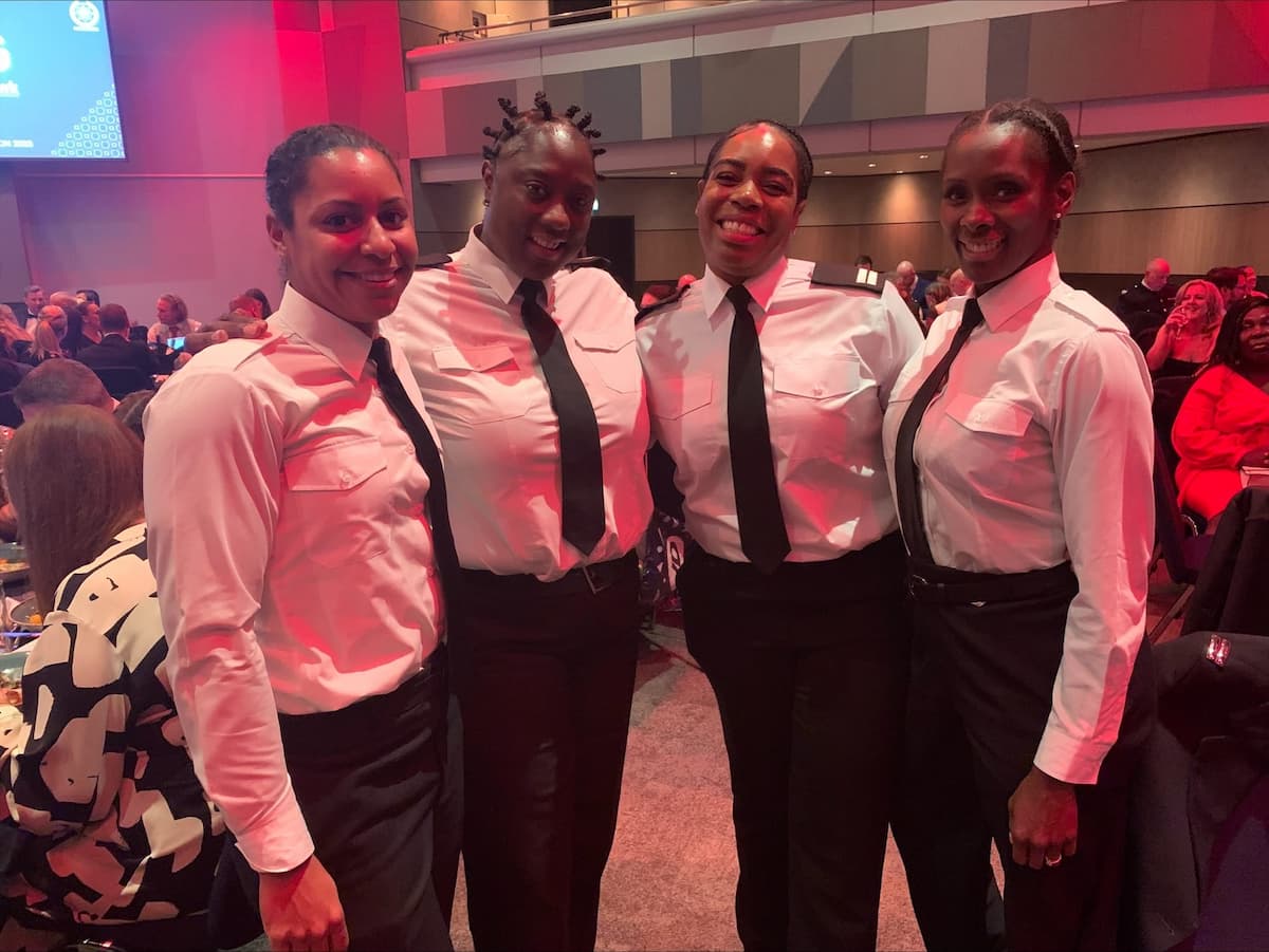 Sam Samuels with three other colleagues, all dressed in fire service uniforms, smiling and posing together at an indoor event.