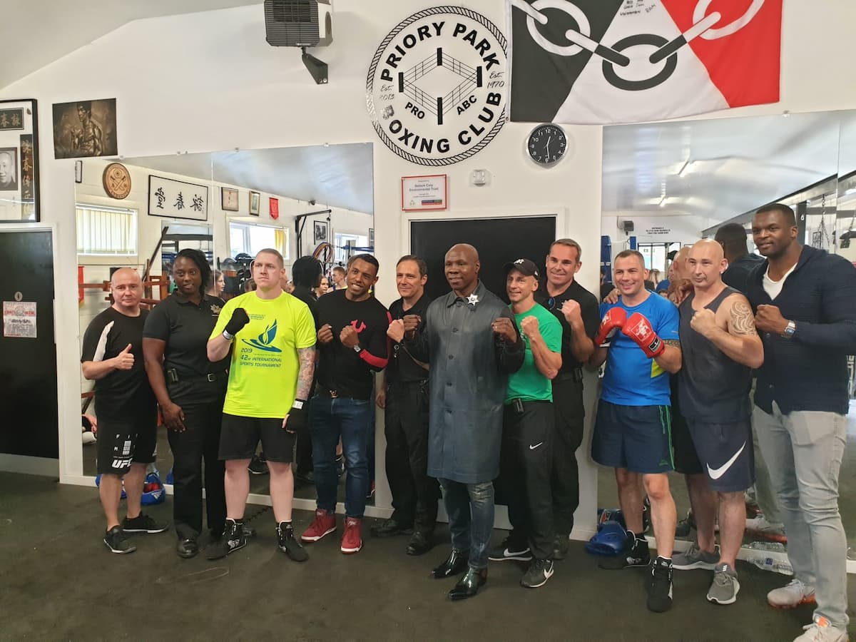 Sam Samuels standing with a group of people in a boxing gym, including boxing professionals and trainers, posing with fists raised in a show of camaraderie.