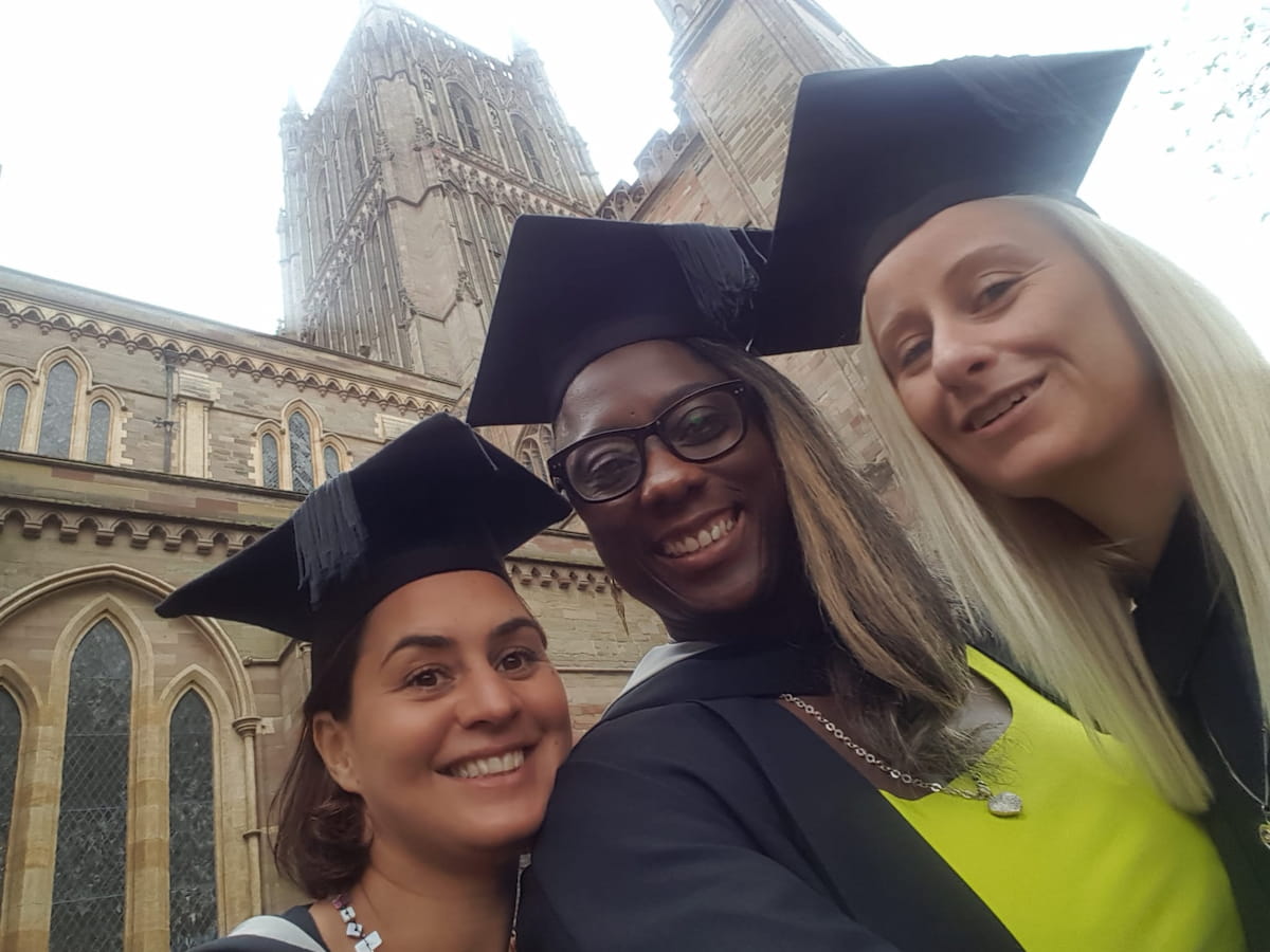 Sam Samuels and two other women in graduation caps and gowns, smiling outside a cathedral after a graduation ceremony.