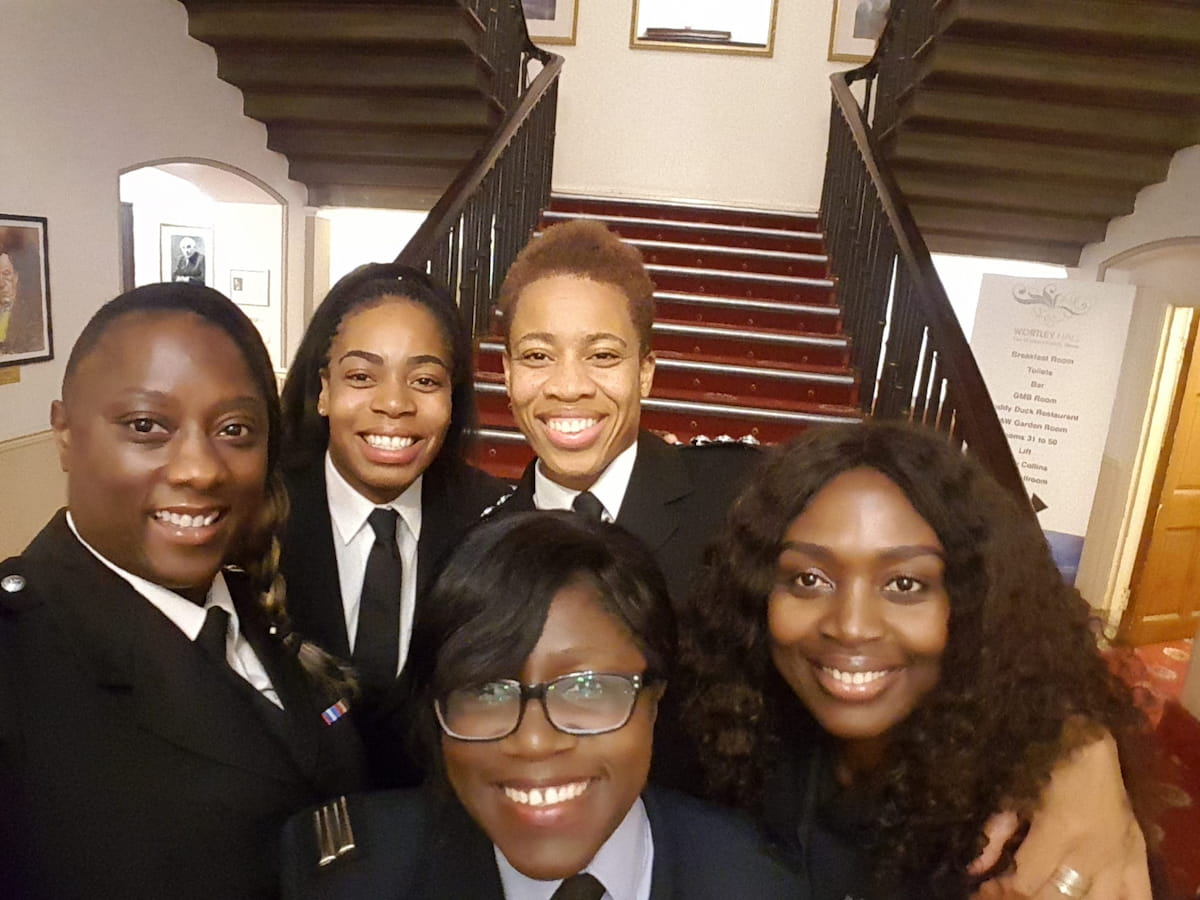 Sam Samuels with four female colleagues from West Midlands Fire Service, all dressed in formal uniforms, smiling together at an indoor event.