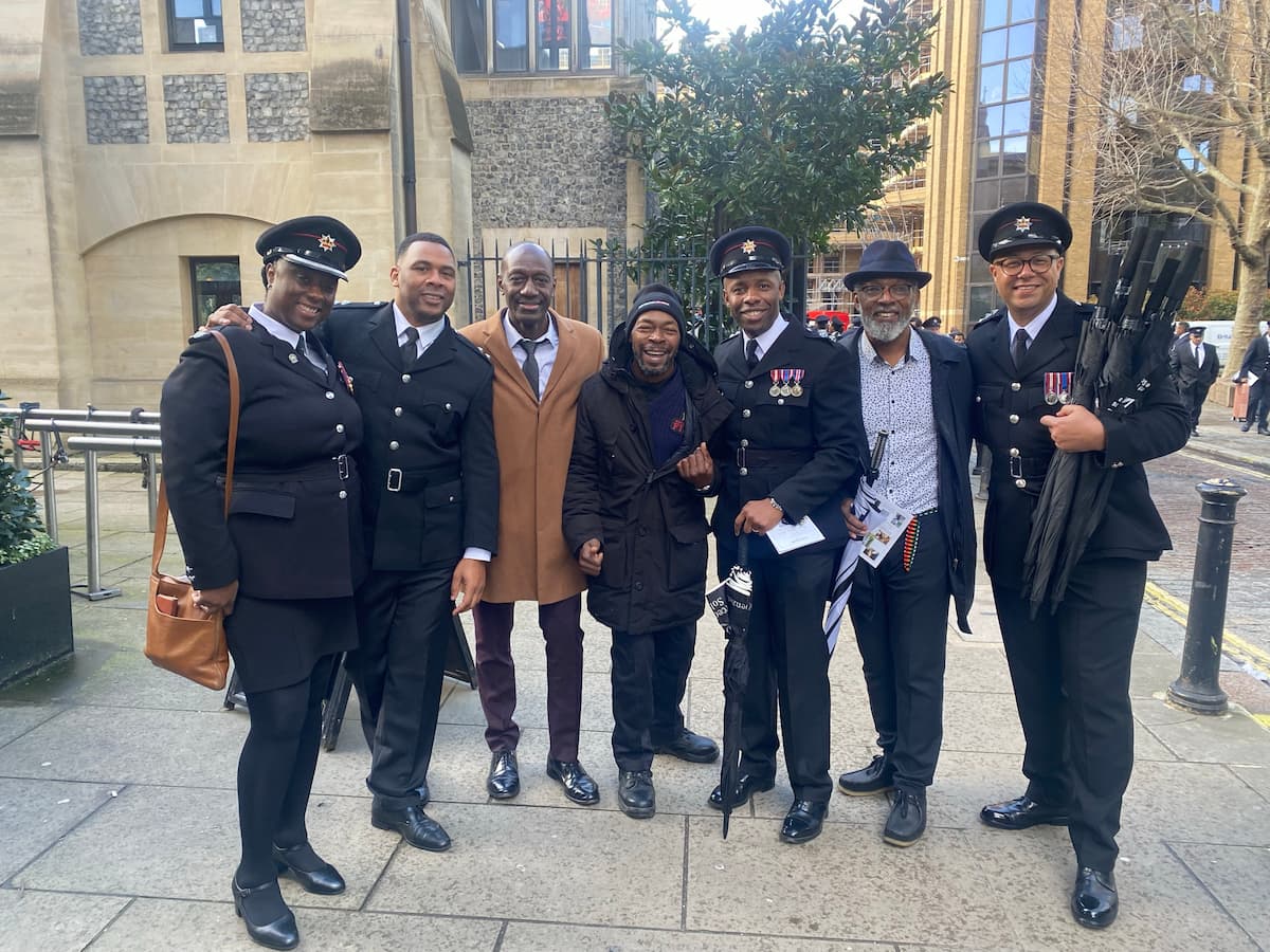 Sam Samuels with a group of West Midlands Fire Service colleagues and community members, gathered outdoors, all dressed formally and posing for the camera.