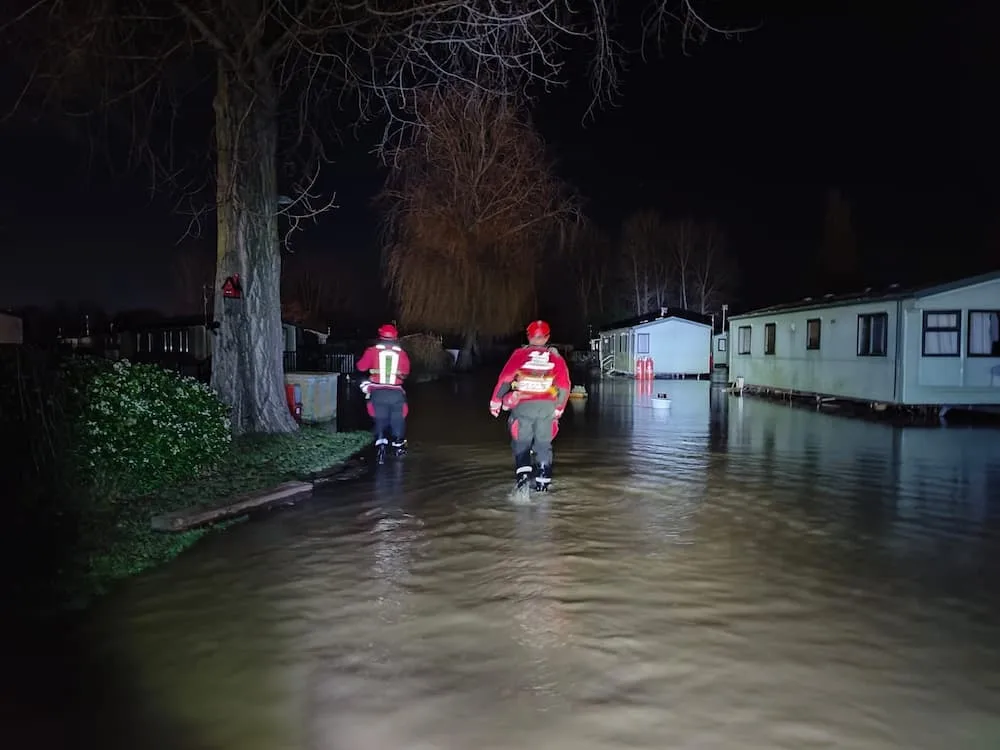 Firefighters walking through flood water with caravans in the background