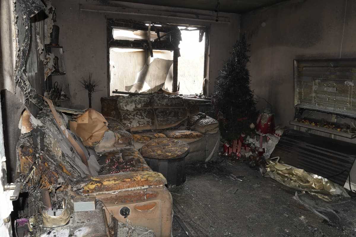 Remains of the living room, some furniture still visible, but smoke and fire damage everywhere